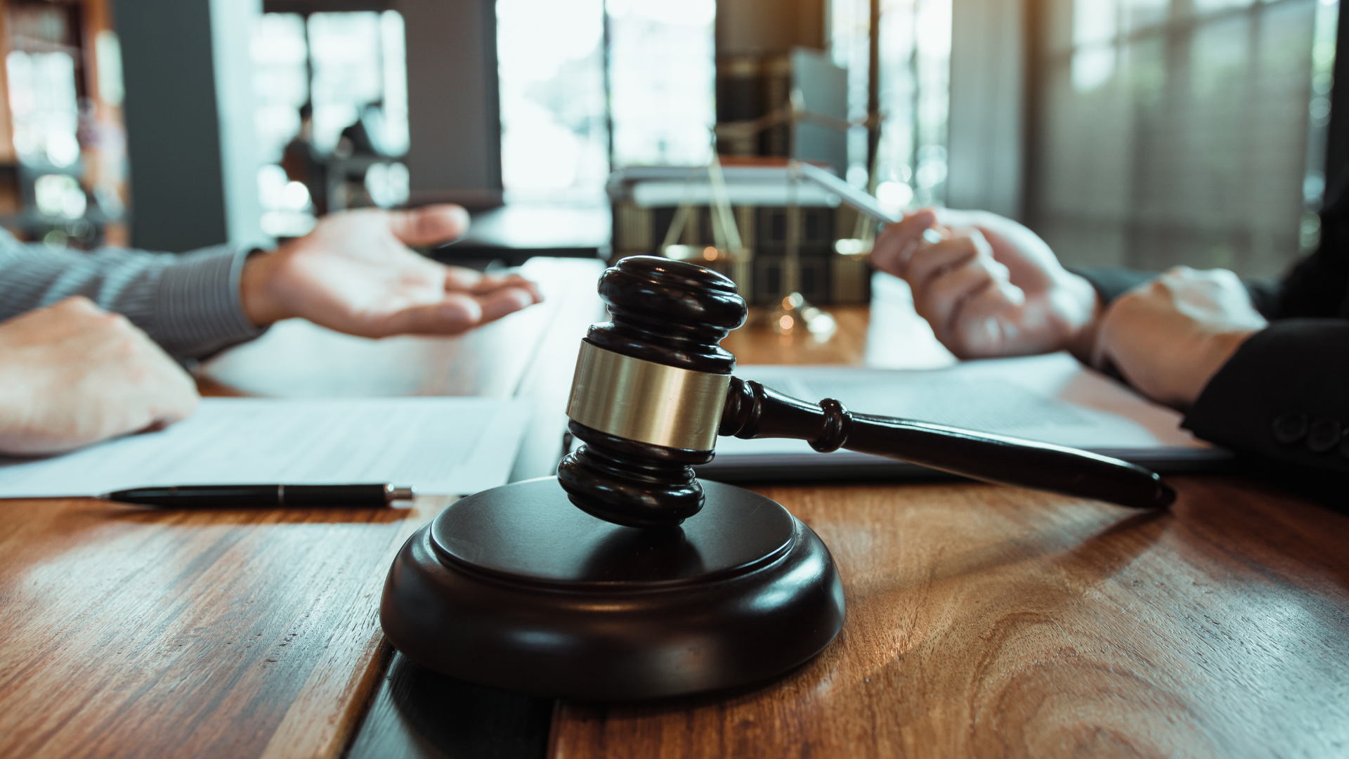 A judge 's gavel is sitting on a wooden table next to two people.