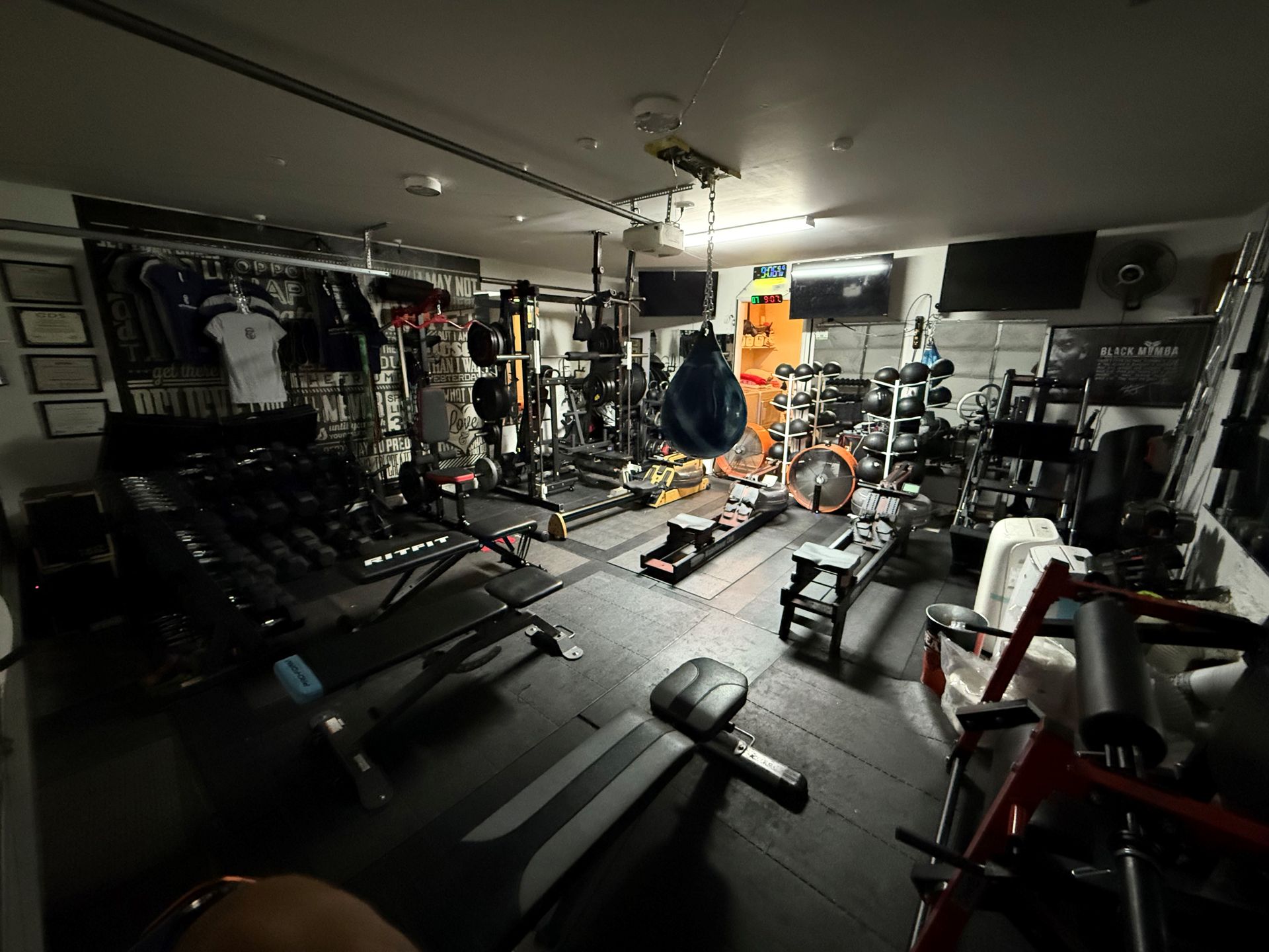 A well-equipped home gym featuring various strength training equipment, weight racks, benches, and a punching bag.