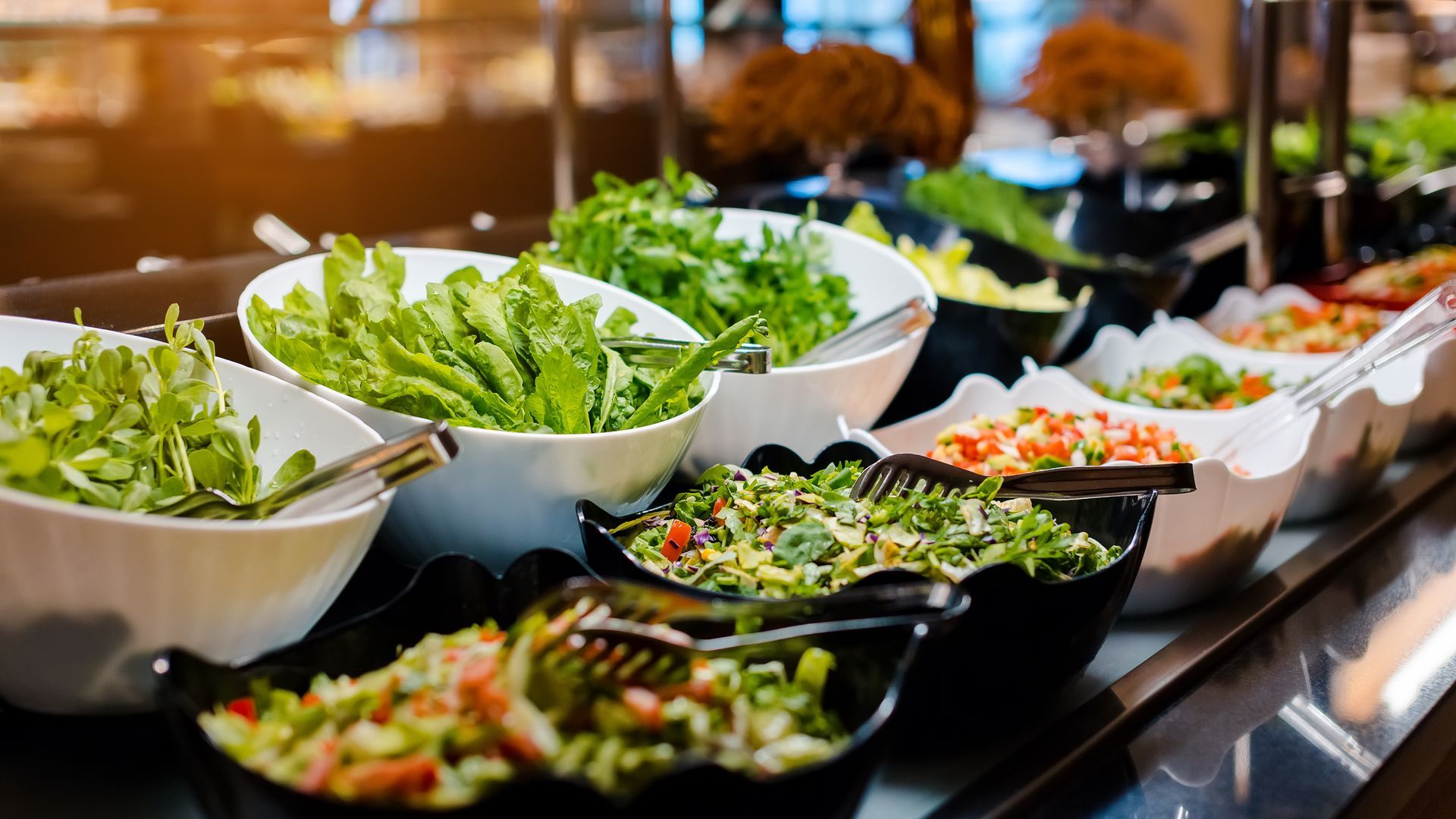 Salatbar mit verschiedenen frischen Gemüsesorten in weißen und schwarzen Schüsseln, servierfertig.