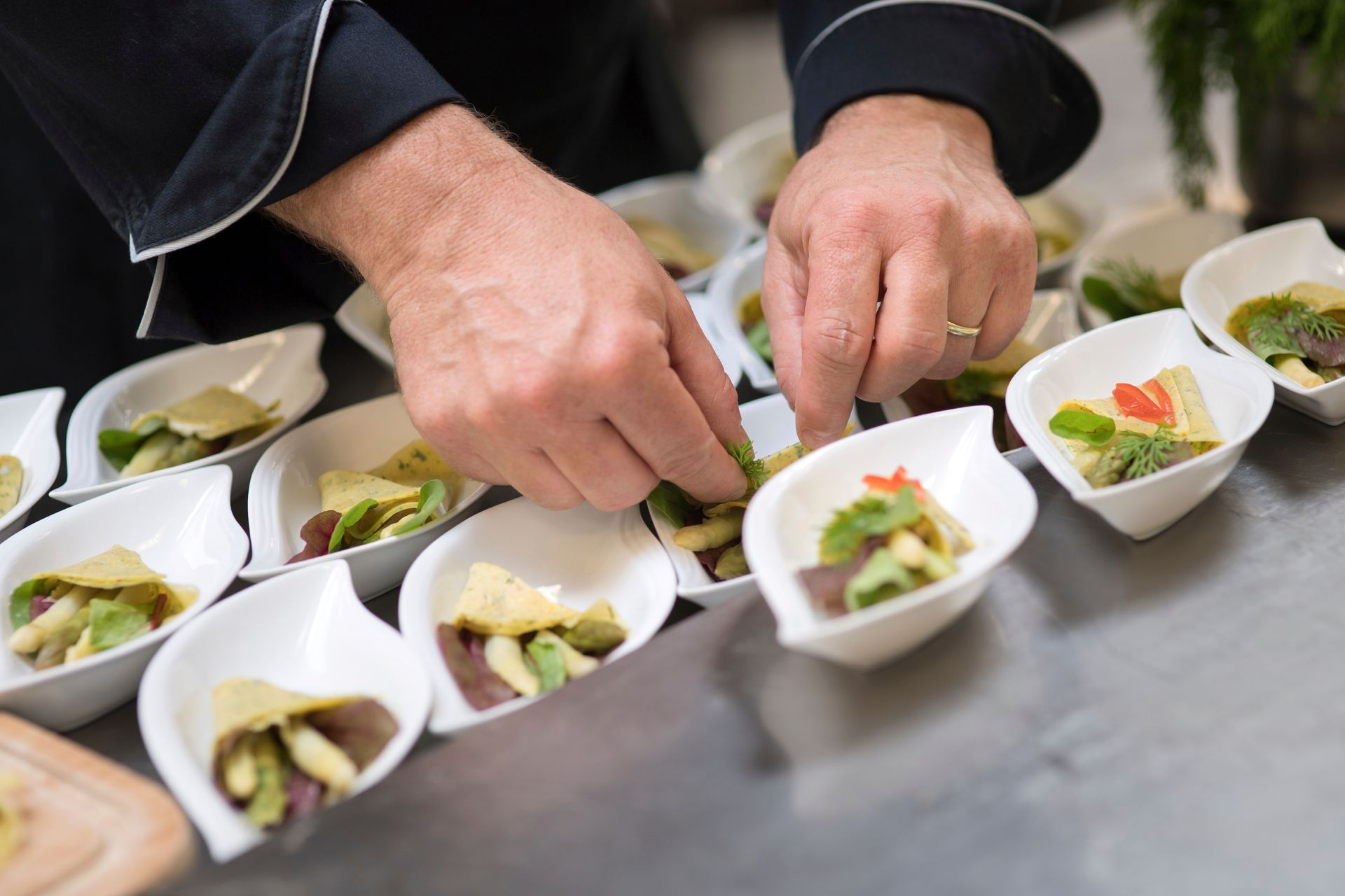 Ein Koch arrangiert Vorspeisen in kleinen weißen Schüsseln auf einer Edelstahlfläche.