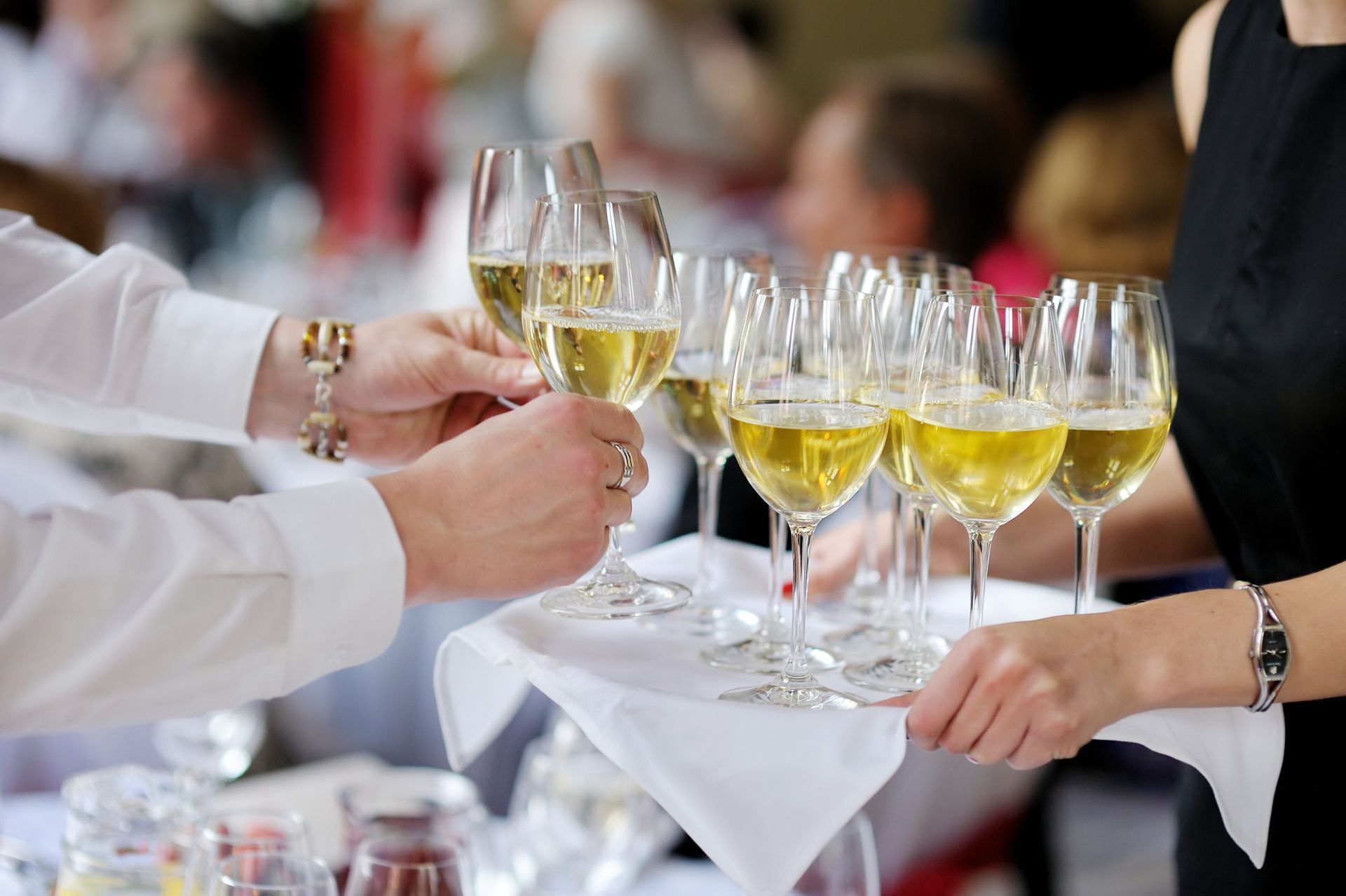 Zwei Personen tragen bei einer Veranstaltung ein Tablett mit Champagnergläsern.