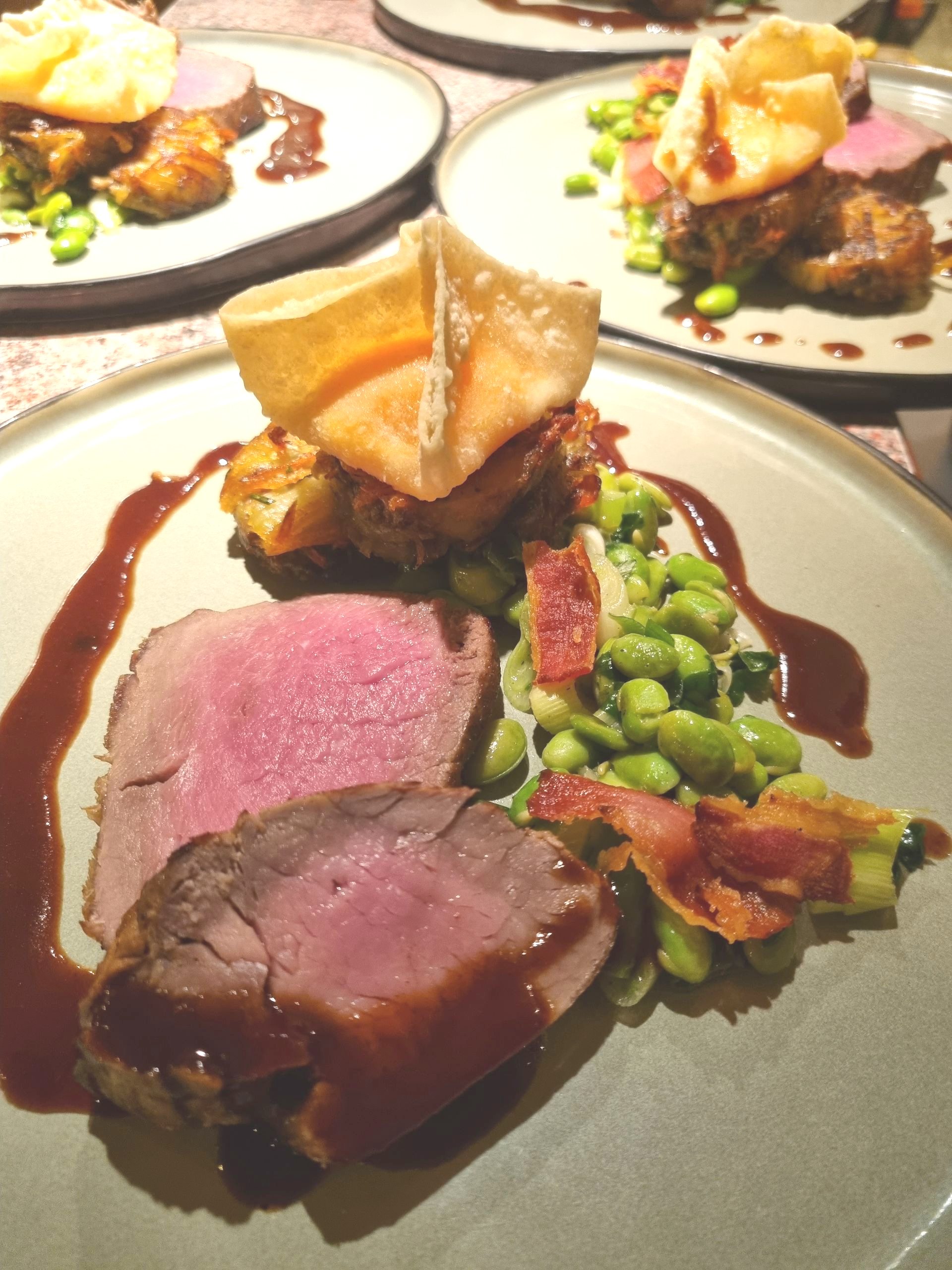Teller mit Essen: gebratenes Fleisch, grüne Bohnen, knusprige Garnitur, Soße.