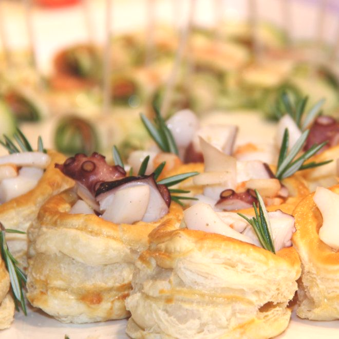 Vorspeisen: Blätterteigförmchen gefüllt mit Oktopus und Kräutern, auf einem Tablett angerichtet.