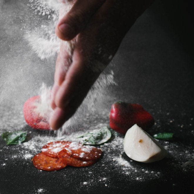 Rote Paprika, Tomaten und Peperoni – werden von Hand mit Mehl auf einer dunklen Oberfläche bestreut.