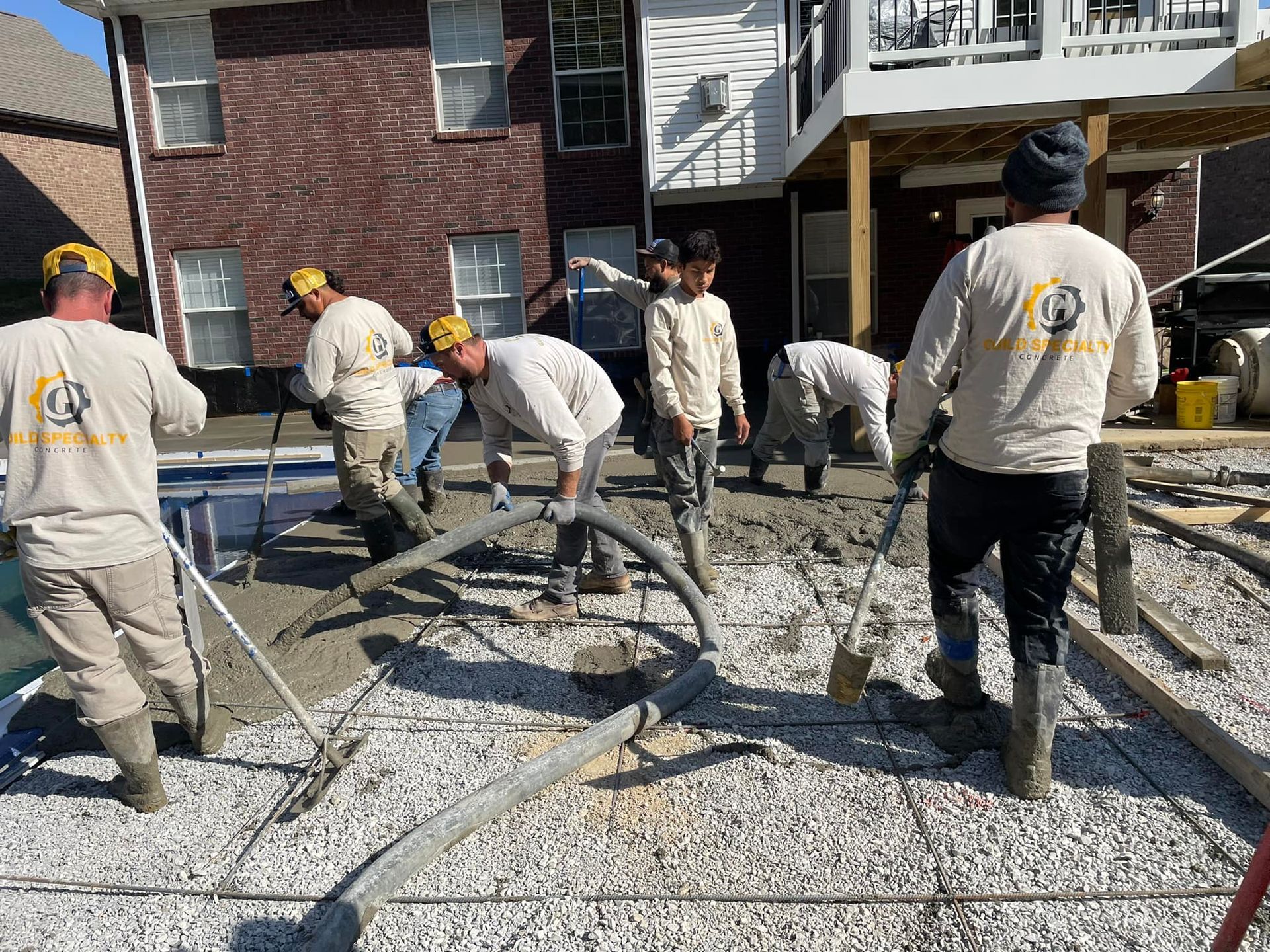 A group of construction workers are working on a concrete floor in front of a house.
