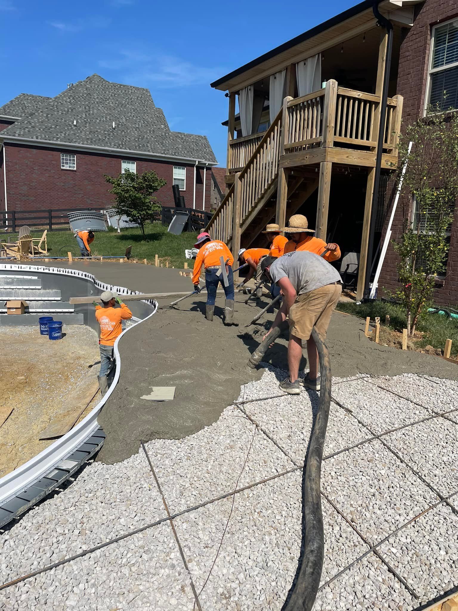 A group of construction workers are working on a concrete driveway in front of a house.