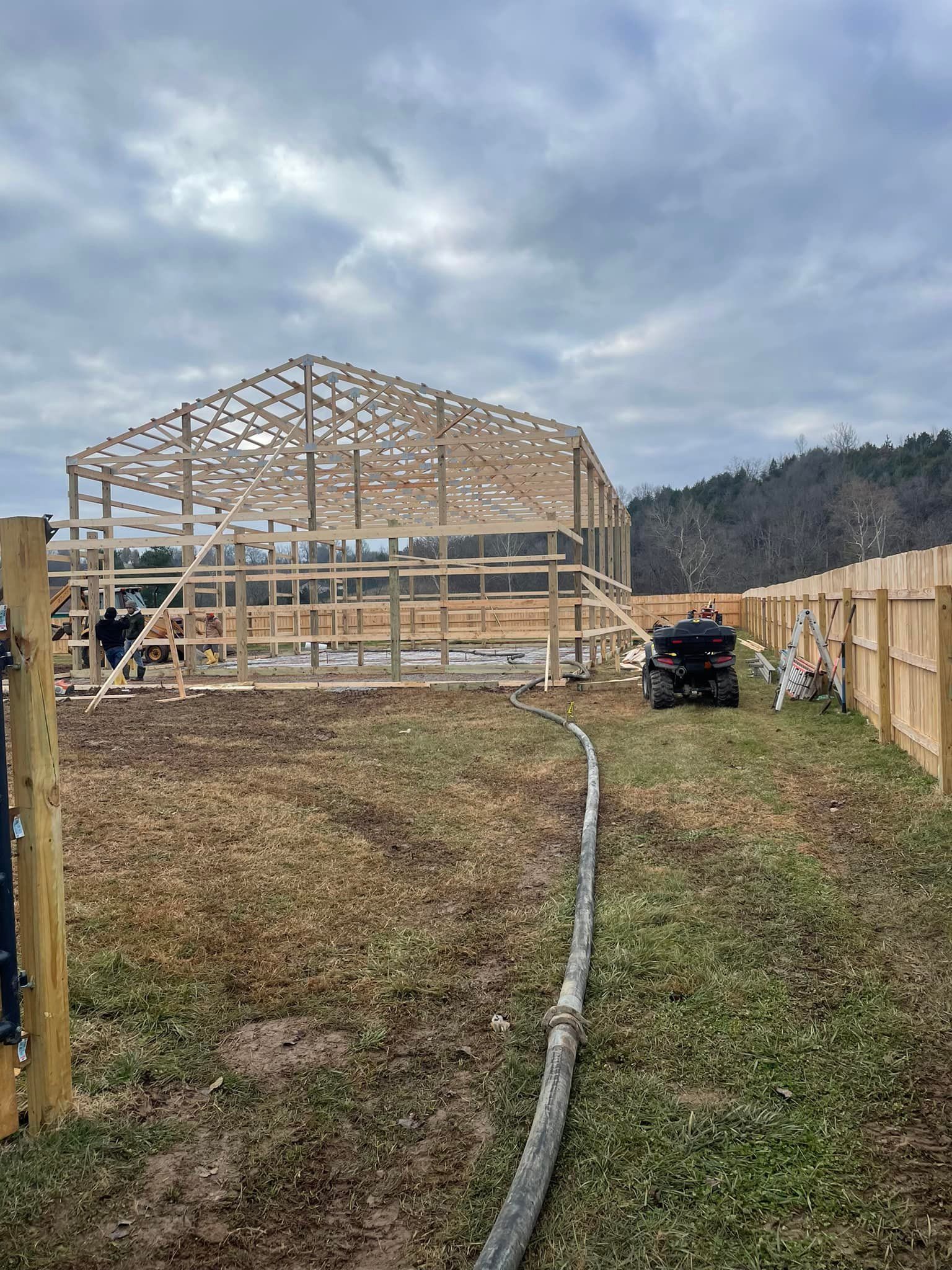 A large wooden building is being built in a field next to a fence.
