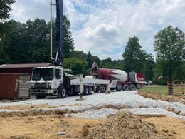 A concrete mixer truck is driving down a dirt road.