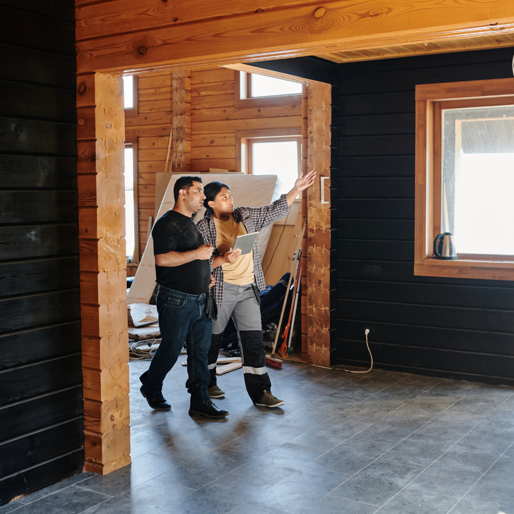 A man and a woman are standing in an empty room looking at a tablet.