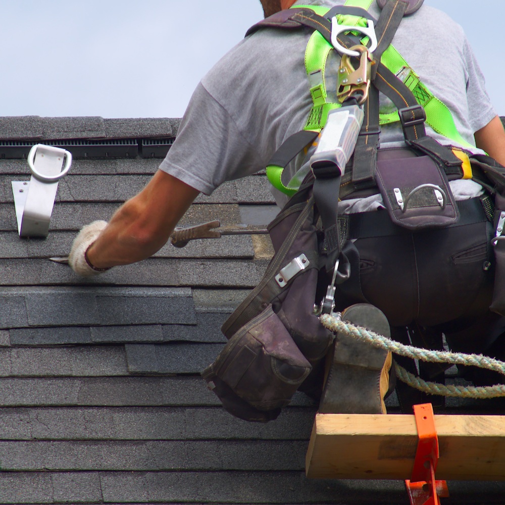 A man wearing a safety harness is working on a roof