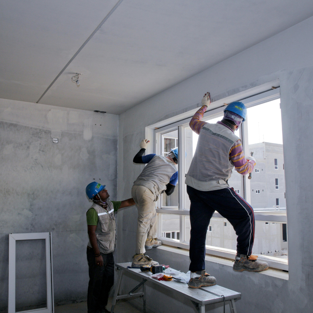 Three men are working on a window in a room