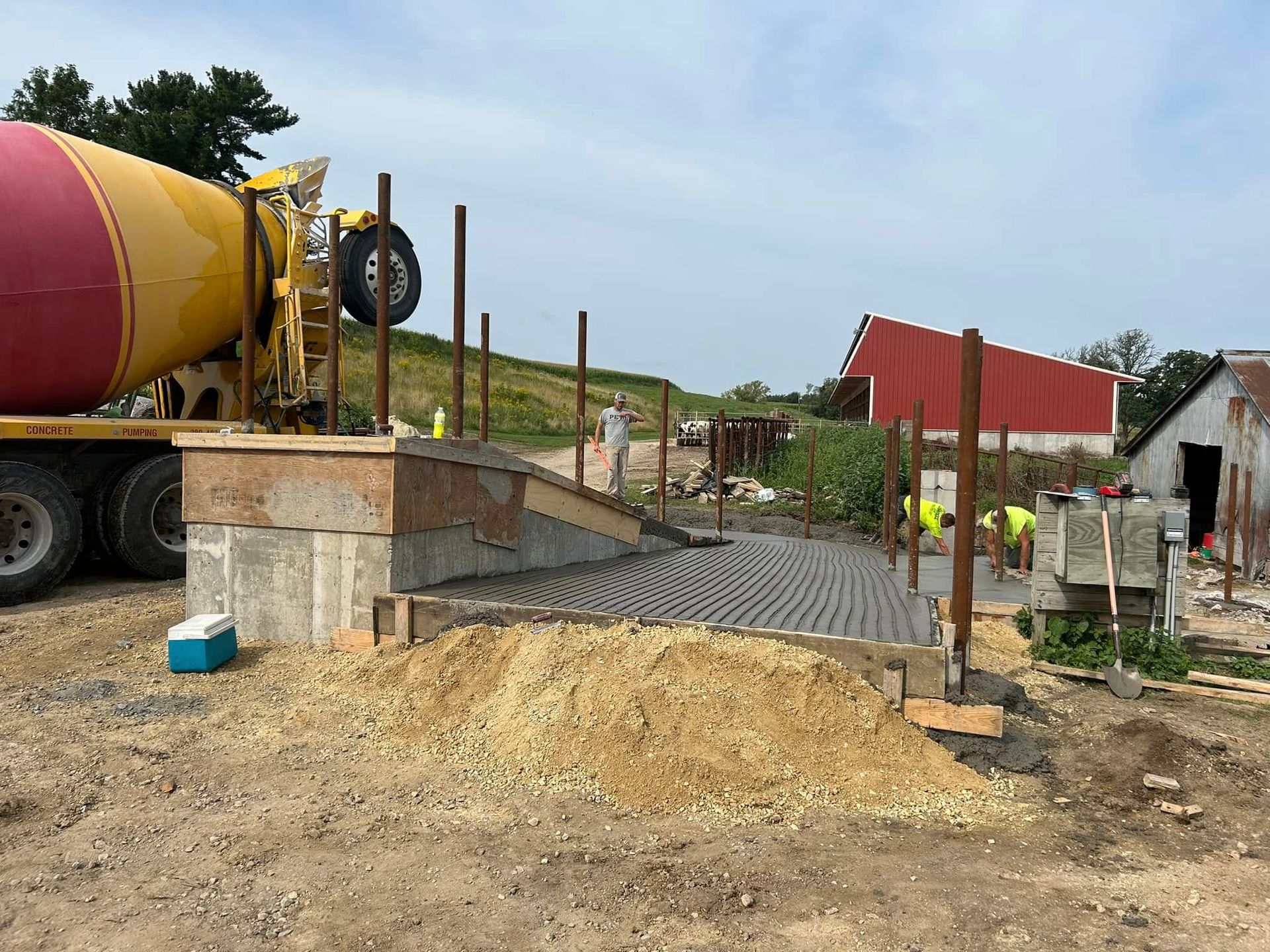 Construction site: concrete pour with a truck, workers, and barn.