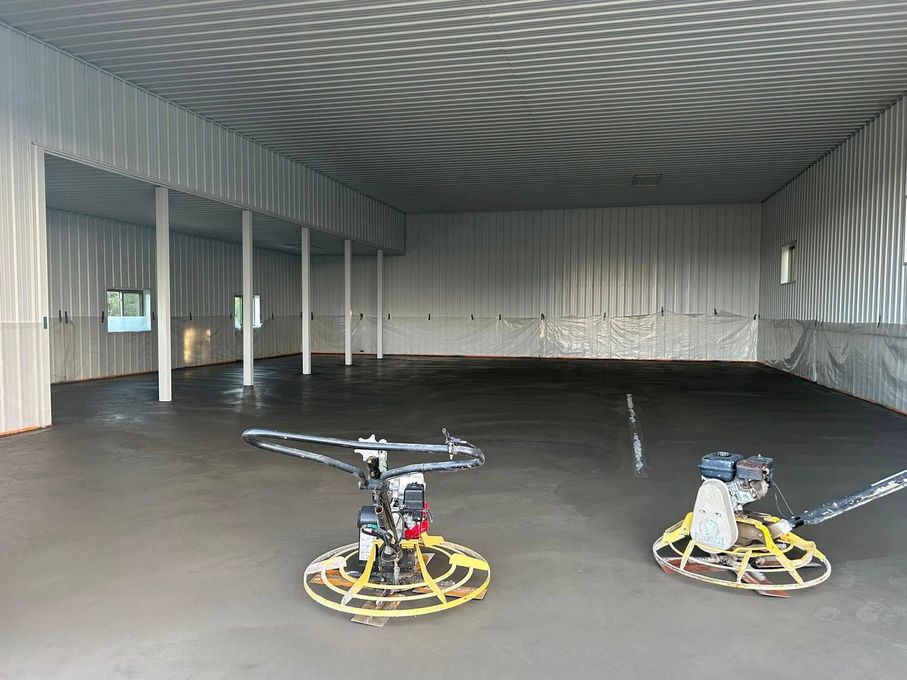 Interior of a large warehouse with freshly poured concrete floor; two power trowels visible.