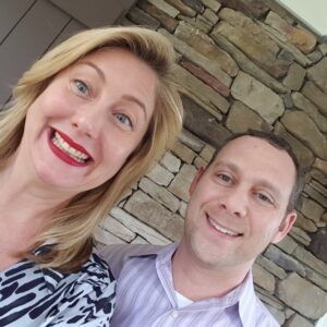 A man and a woman are smiling for a picture in front of a stone wall.