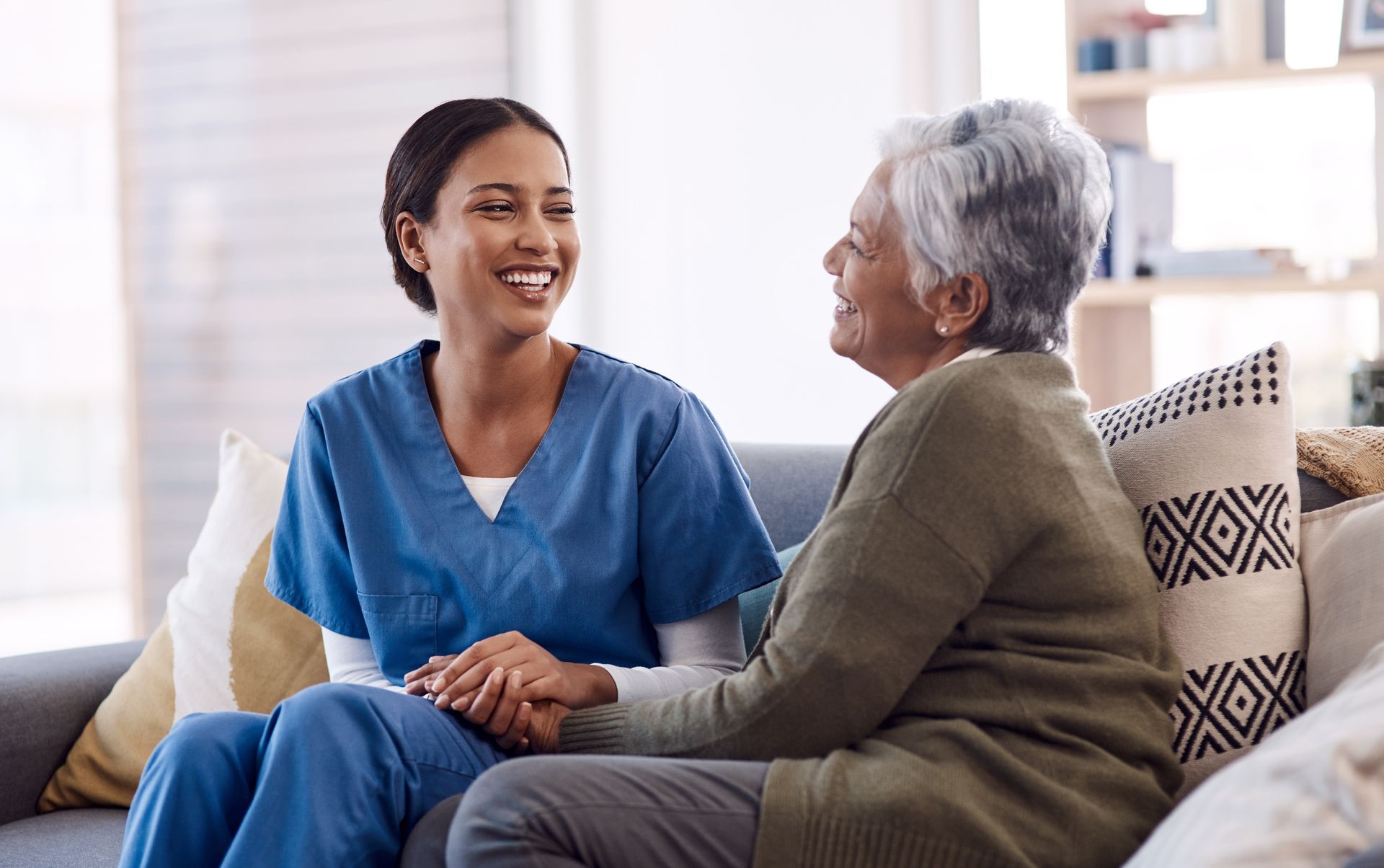 Caregiver holding hands with an older woman while sitting together on a couch.