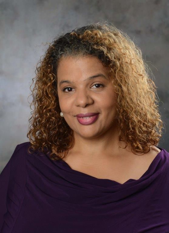 A woman with curly hair is wearing a purple shirt and smiling for the camera.