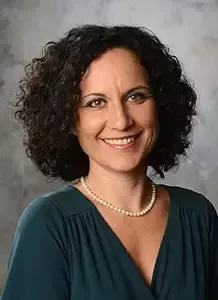 A woman with curly hair and a pearl necklace is smiling for the camera.