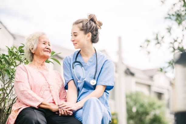Nurse in blue scrubs comforting elderly woman in garden, healthcare and senior care concept
