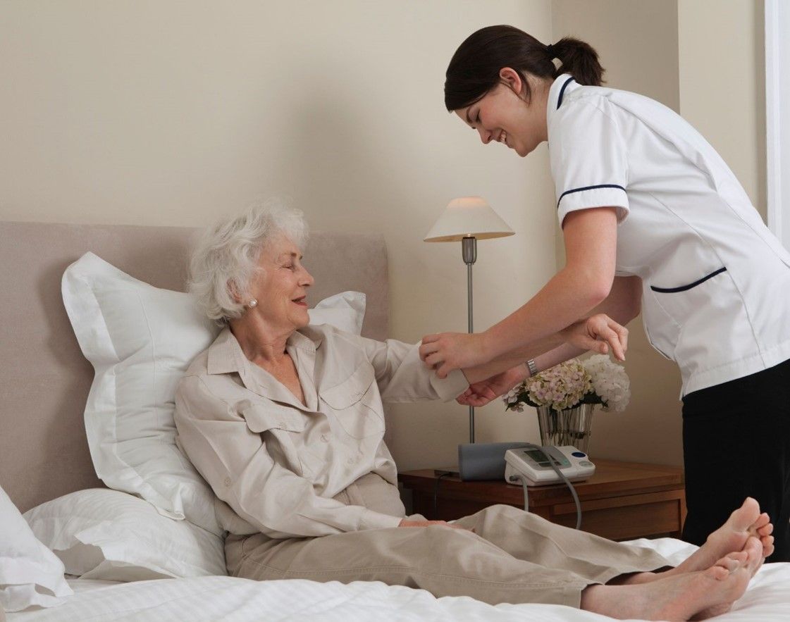 An in-home caregiver, wearing a blue uniform, hugging a senior.