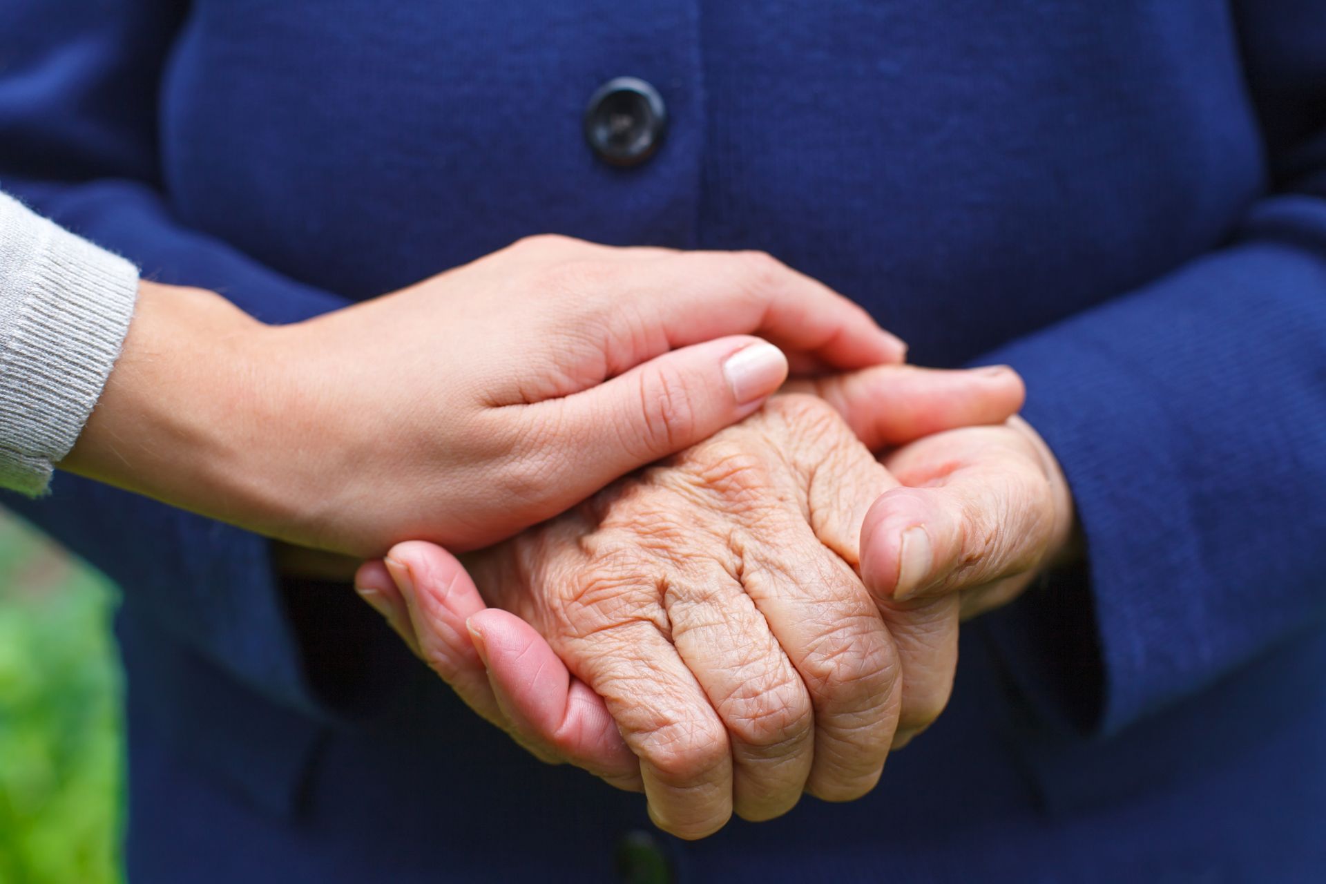 A woman is holding the hand of an older woman in a blue coat.