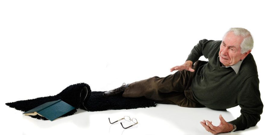 An elderly man is laying on the floor with a book and glasses on the floor.