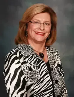 A woman wearing a zebra print jacket and glasses is smiling for the camera.