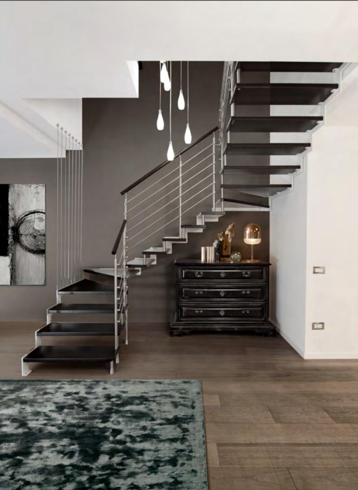 Scala moderna in un interno minimalista con gradini in legno scuro, lampade a sospensione e una cassettiera nera.