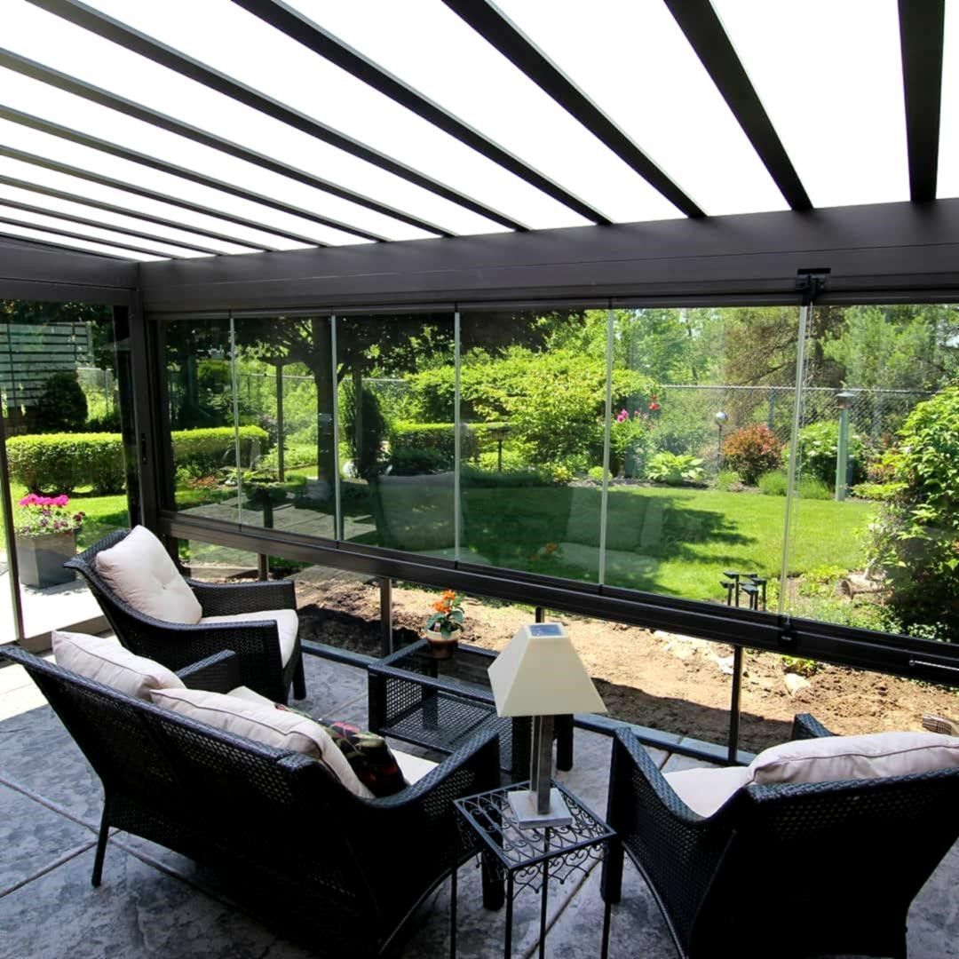 Patio coperto con sedie in vimini nere e ringhiera in vetro che si affaccia su un rigoglioso giardino verde.