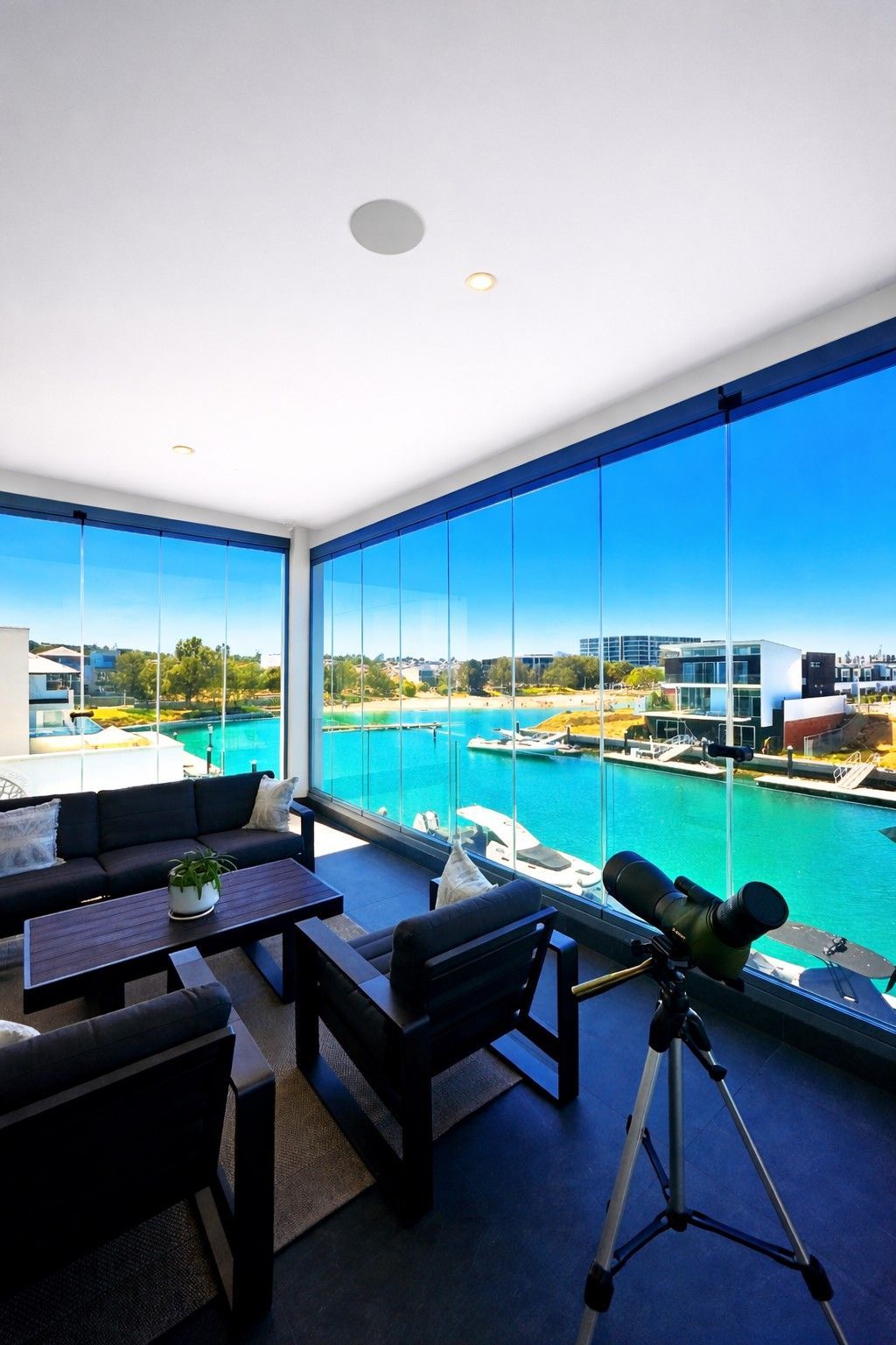Moderno balcone sul lungomare con sedie nere, telescopio e vista panoramica sul porto turchese.