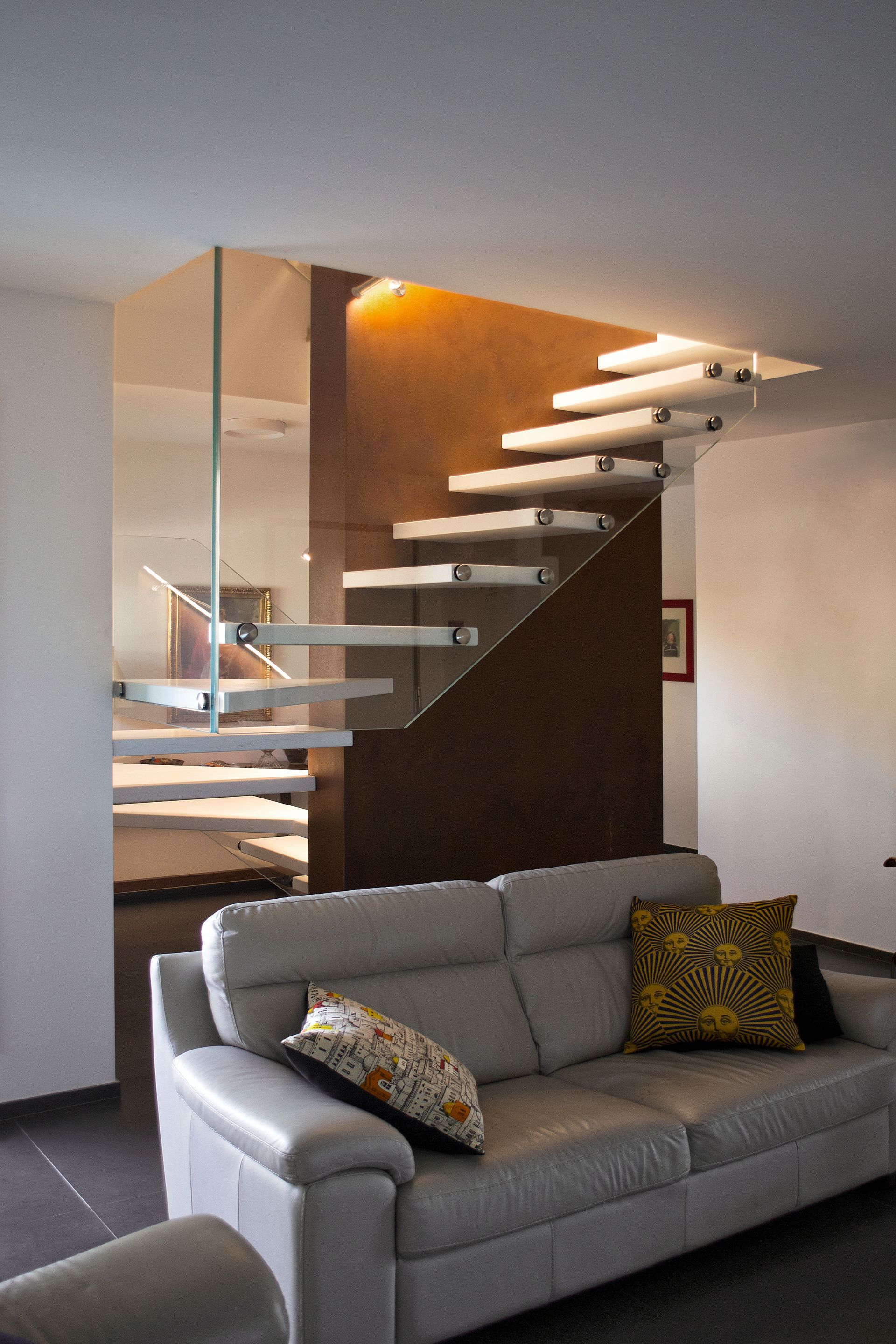Soggiorno moderno con divano grigio e scala sospesa alle sue spalle.