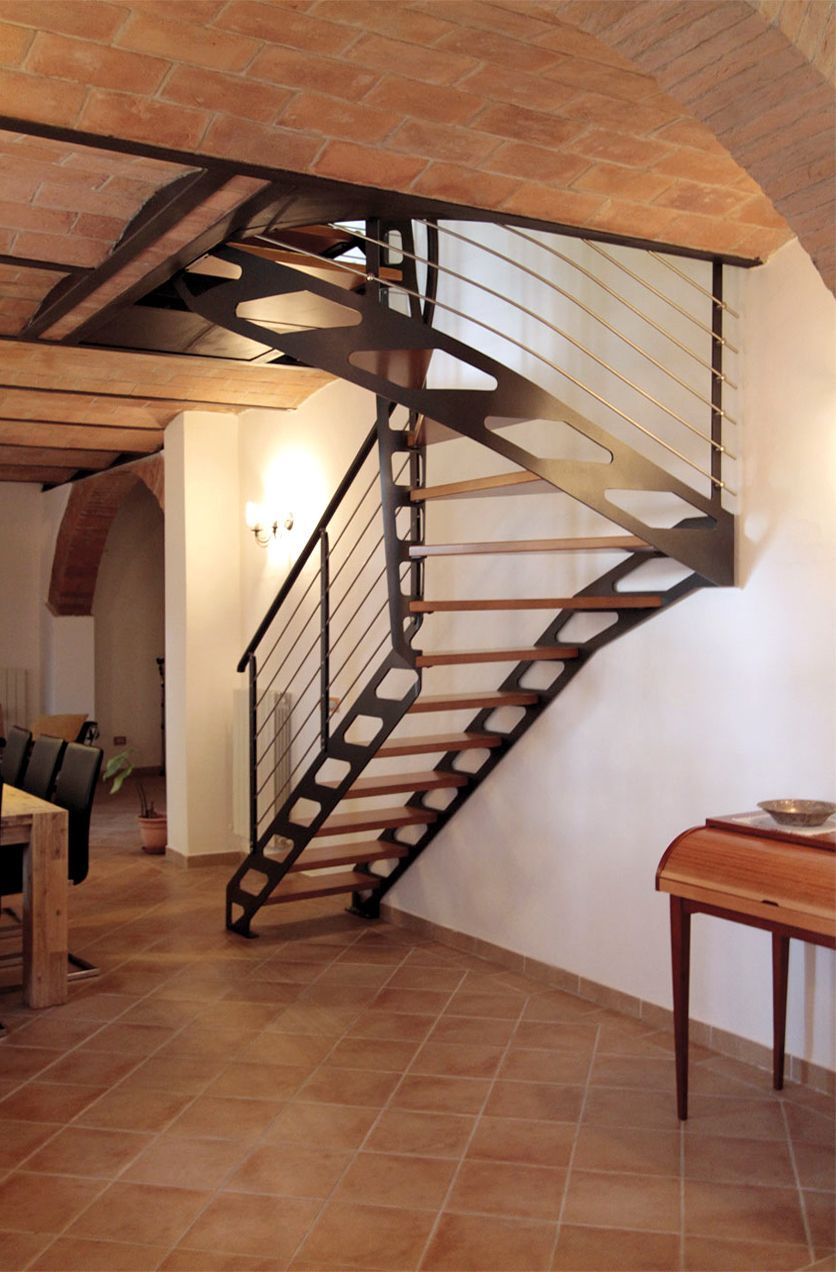 Scala a chiocciola interna con gradini in legno, ringhiera scura e soffitto a volta in mattoni in una stanza piastrellata.