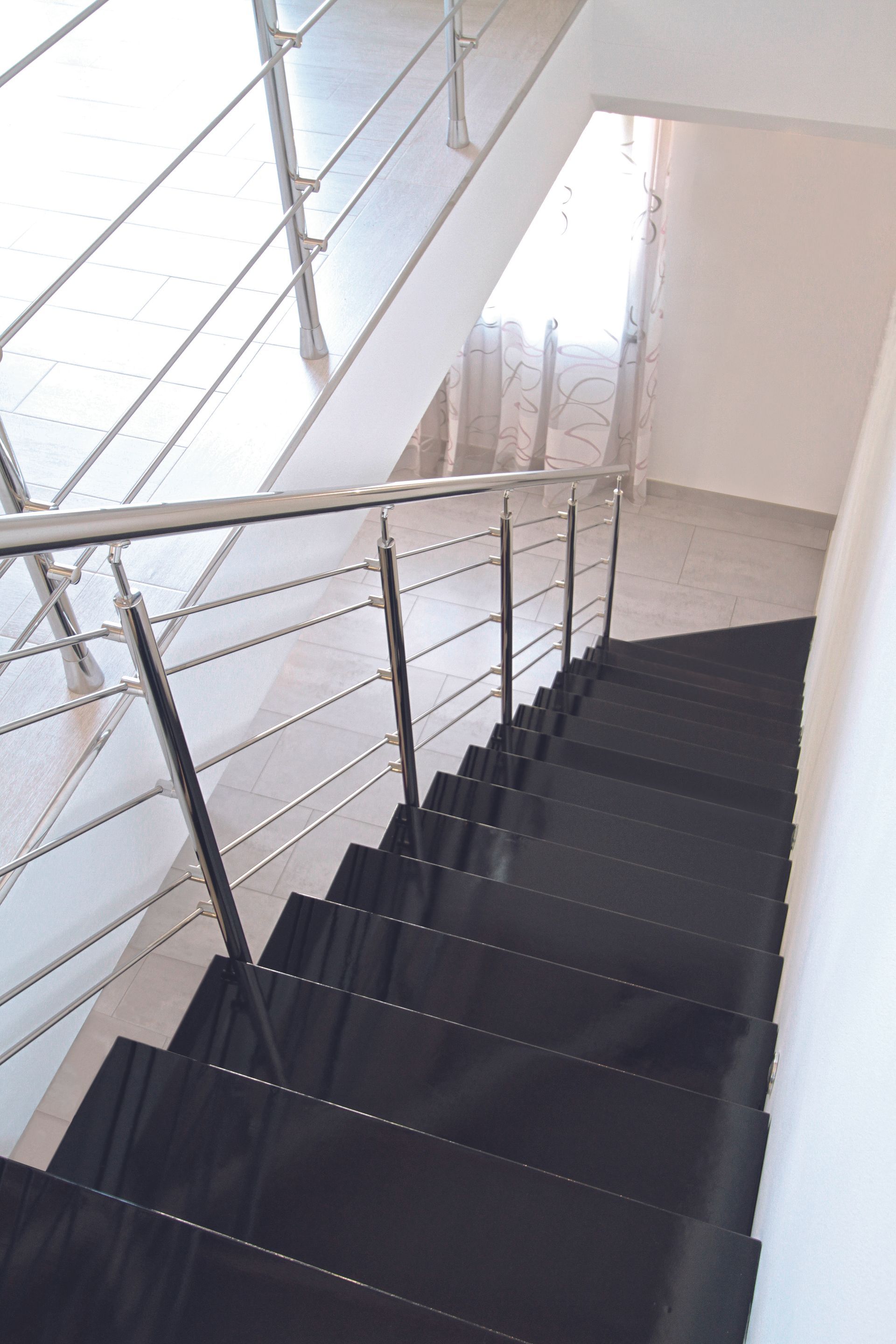 Scala interna moderna con gradini scuri e ringhiera in acciaio inox lungo una parete bianca.