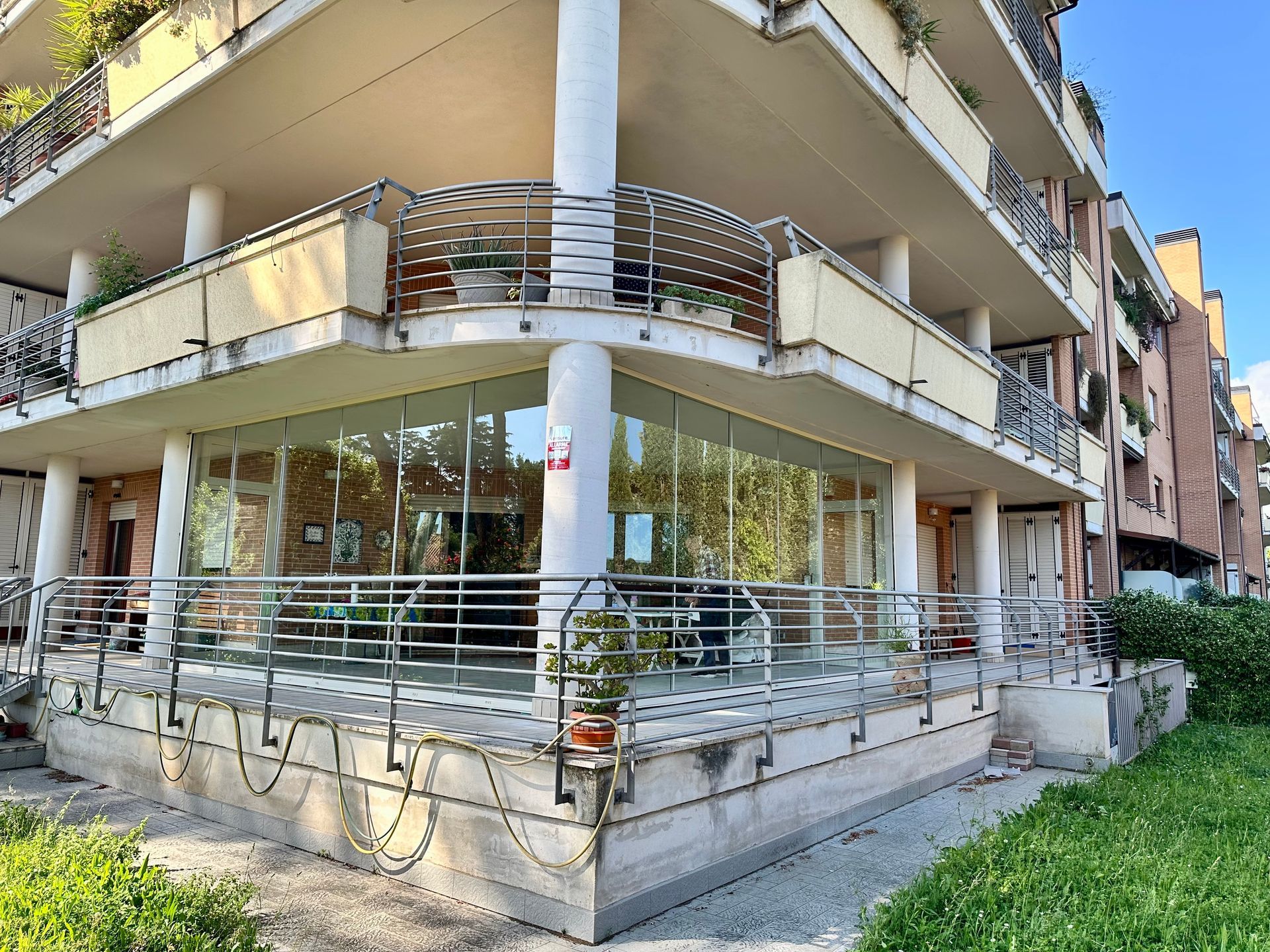 Area esterna coperta del caffè con lunghi tavoli e sedie in legno accanto a una parete di vetro.