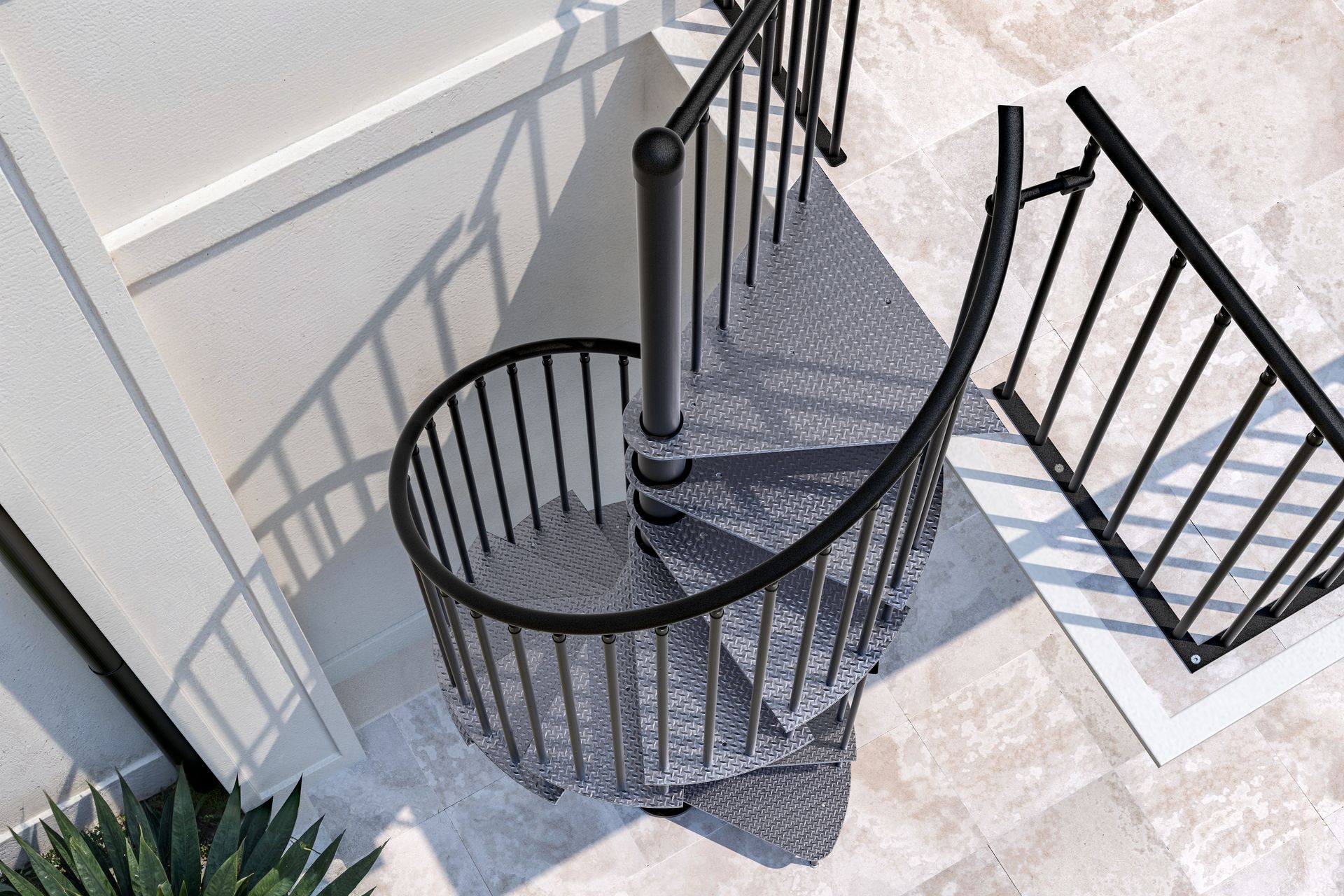 Scala a chiocciola curva in metallo nero accanto a una parete bianca e a un patio piastrellato.