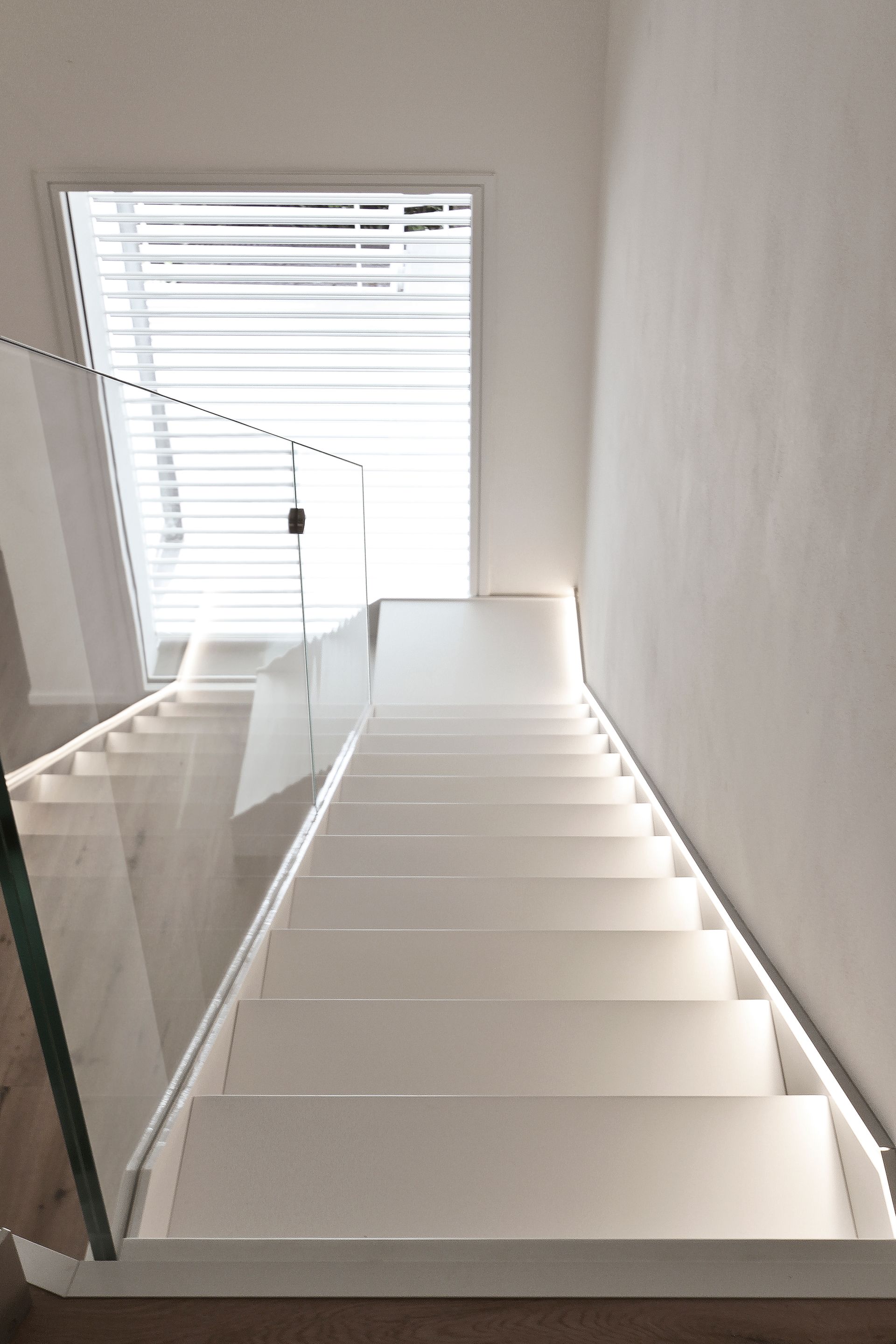 Scala moderna bianca con ringhiera in vetro accanto a un'alta finestra e tende.