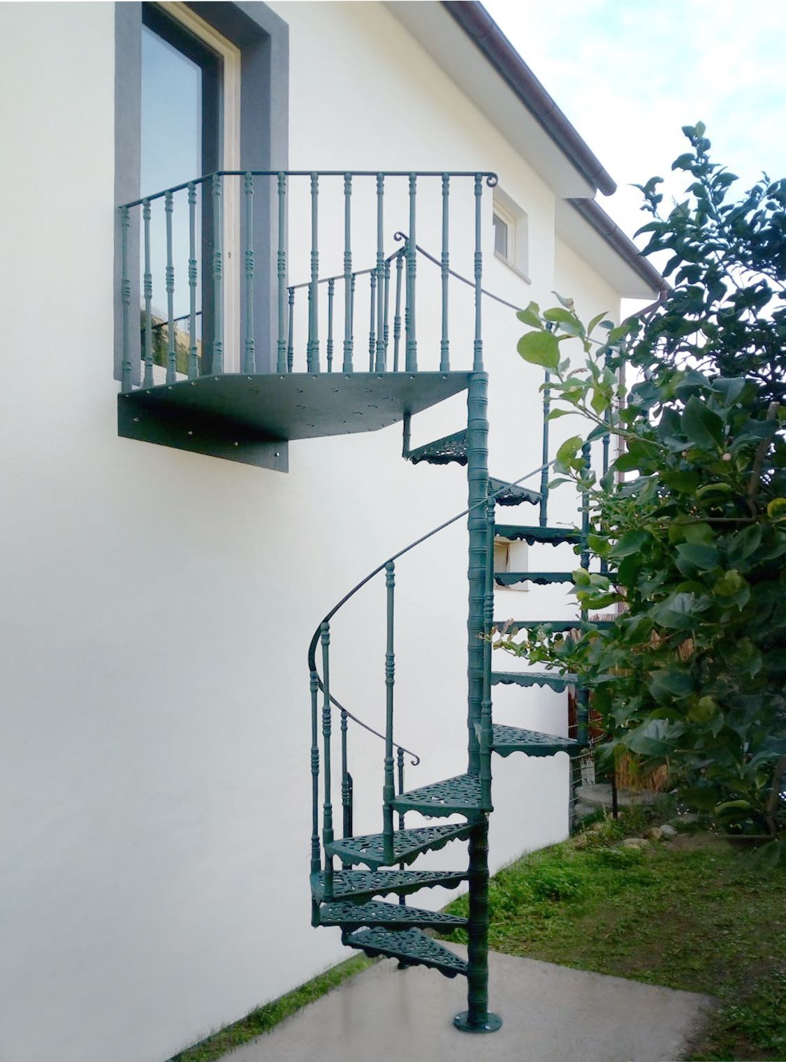 Scala a chiocciola esterna accanto a una casa bianca con un piccolo balcone e una ringhiera verde.
