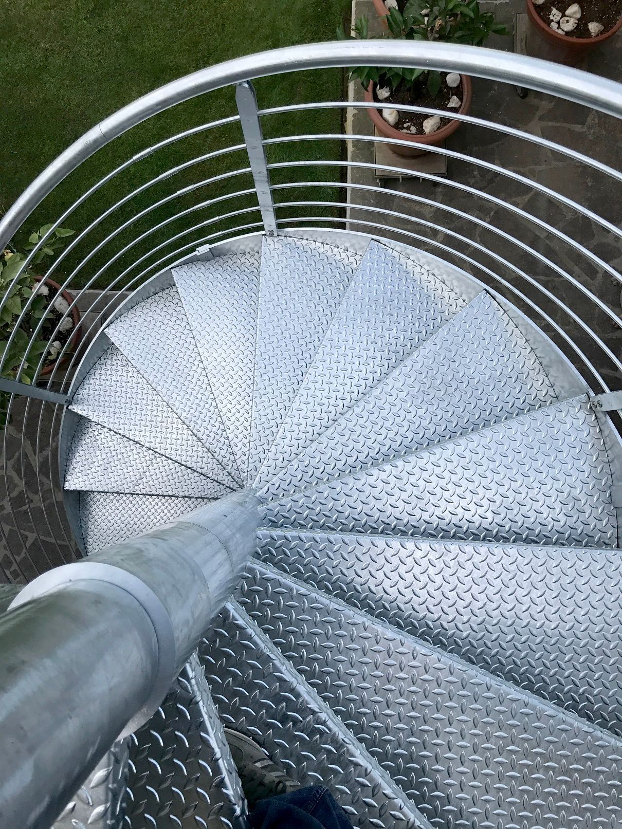 Scala a chiocciola in metallo vista dall'alto, con ringhiere grigie e gradini in lamiera diamantata.