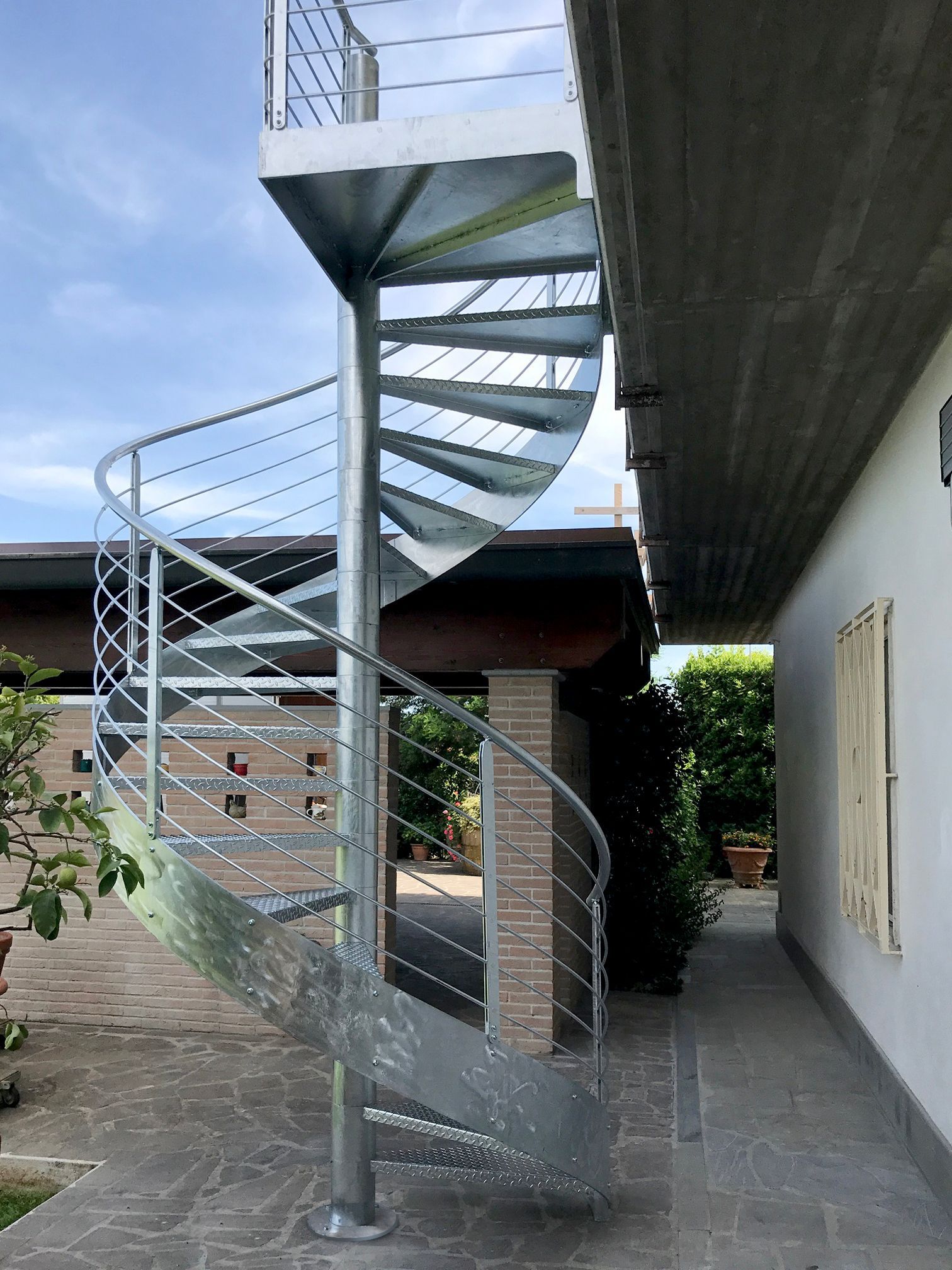 Scala a chiocciola esterna in metallo accanto a un edificio, vista dal basso in un cortile.