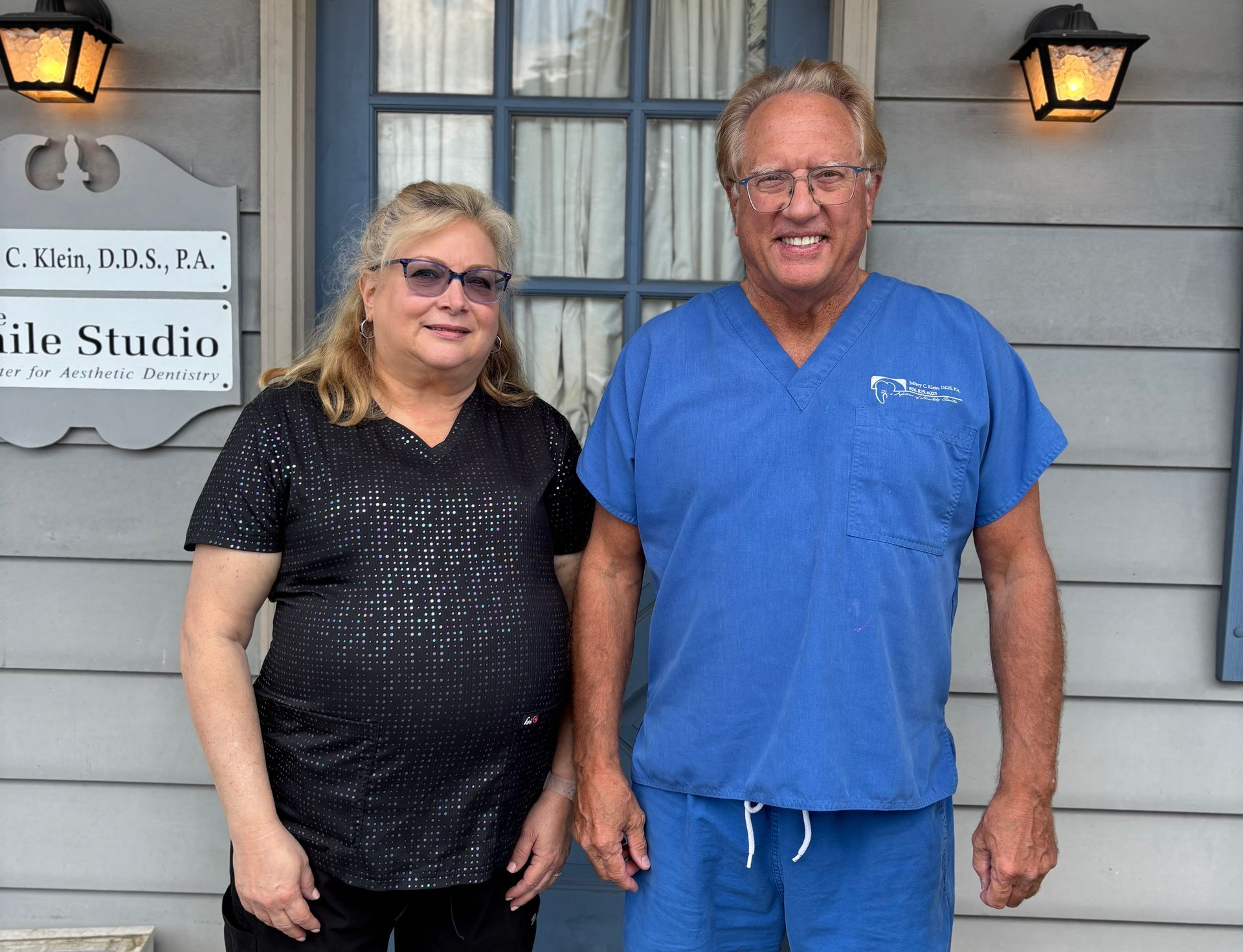 Woman and man in front of a dental office. The man wears blue scrubs. They both smile.