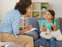 Counselor talking with a girl on a couch; the girl holds a stuffed toy and gestures while listening.