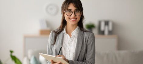 Smiling woman with glasses holding a tablet in a bright office