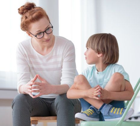 Woman talking with a child sitting on a chair in a bright room.