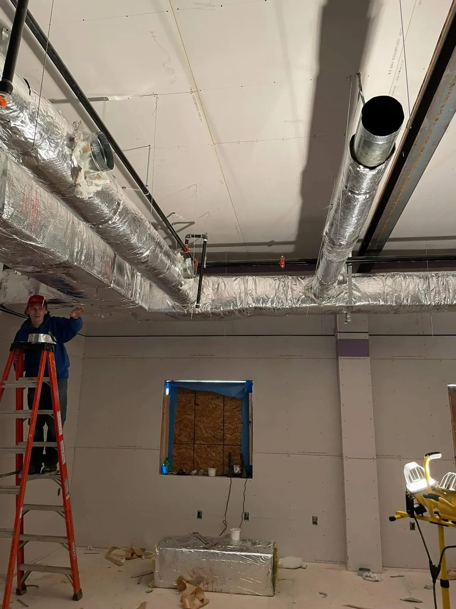 A man on a ladder is working on the ceiling of a building.