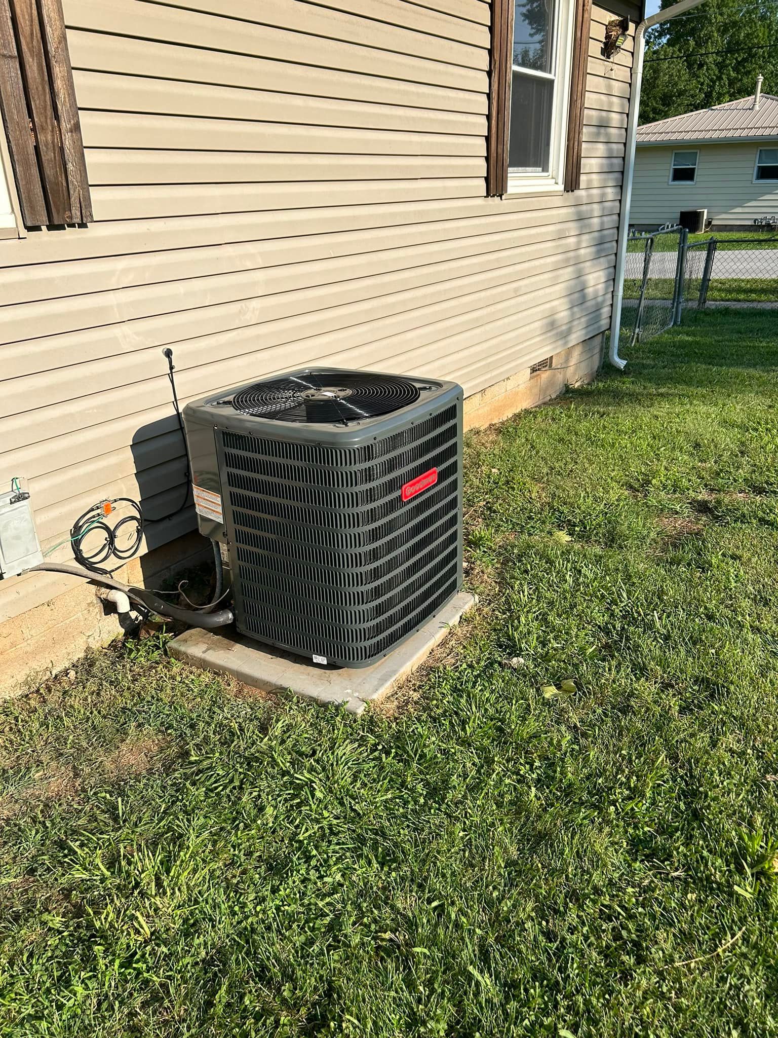 An air conditioner is sitting in the grass next to a house.