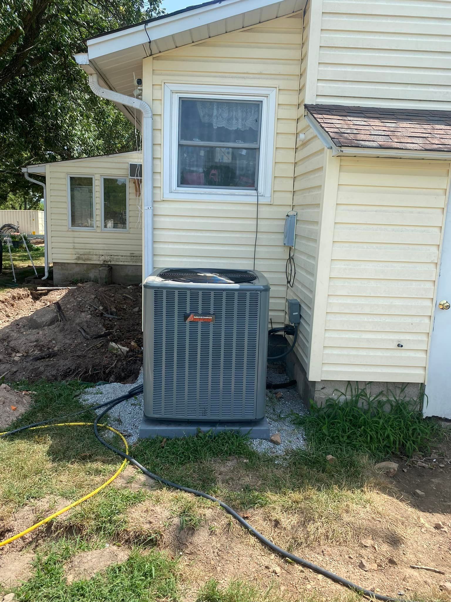 An air conditioner is sitting on the side of a house next to a window.