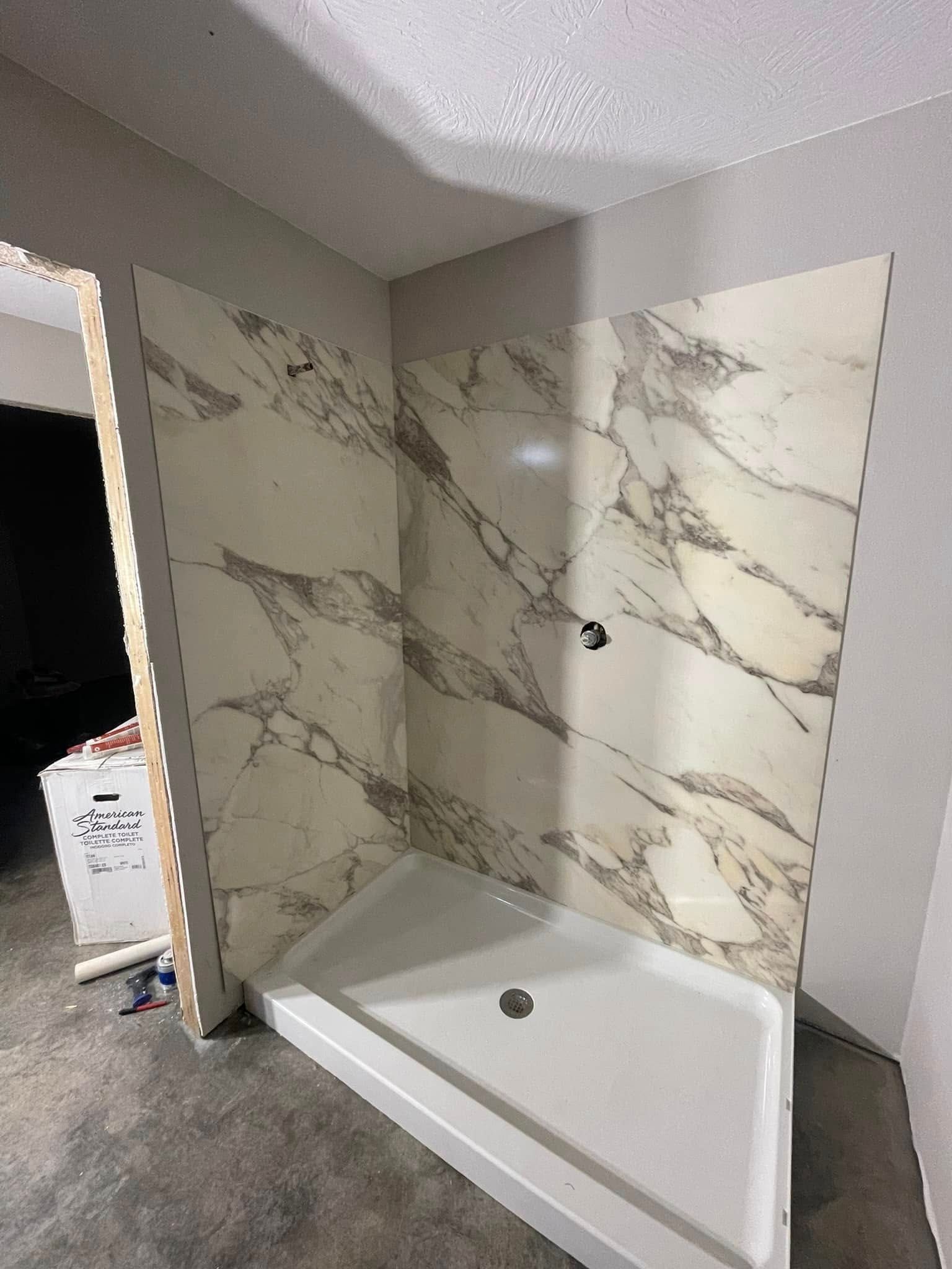 A shower stall in a bathroom with marble tiles on the wall.