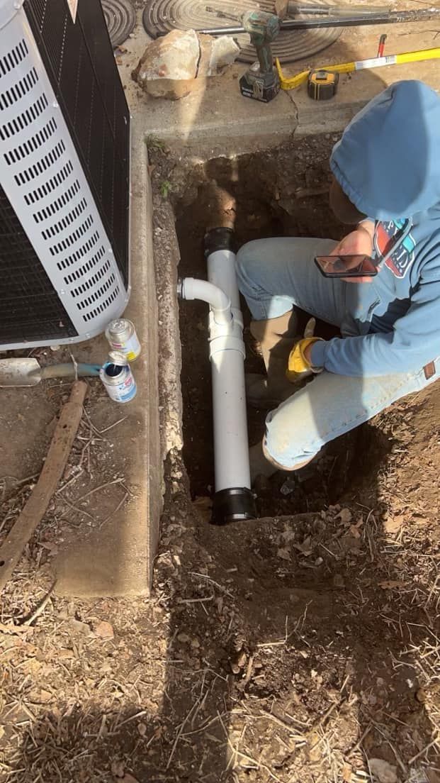 A man is kneeling down in the dirt fixing a pipe.