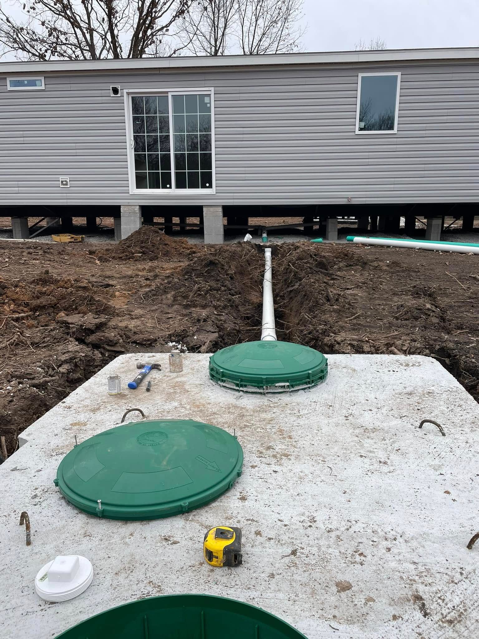 A septic tank is sitting in the dirt in front of a house.