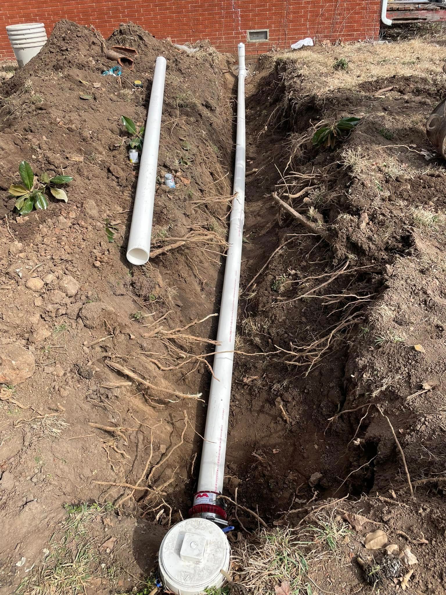 Two white pipes are laying in the dirt in a hole.
