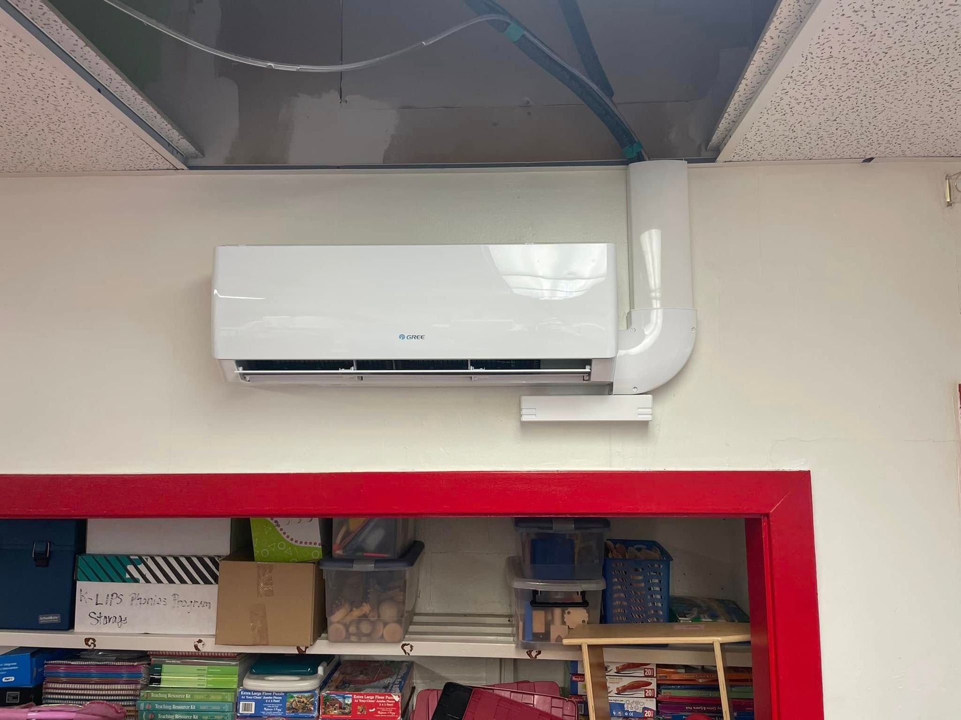 A white air conditioner is hanging from the ceiling in a classroom